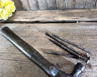 May include: A vintage claw hammer with a wooden handle and a metal head. The hammer is lying on a wooden surface with several rusty nails scattered around it.