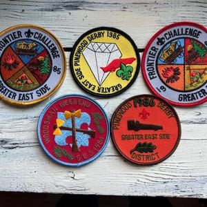 May include: Five colorful embroidered patches with the text "Frontier Challenge", "Pinewood Derby", "Woodsman Weekend", "Pinewood Derby", and "Frontier Challenge".