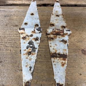 May include: Two antique white metal hinges with rust spots. The hinges are triangular in shape and have multiple holes for attaching to a door or gate.