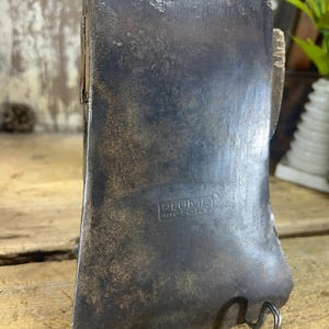 May include: A vintage axe head with a dark, weathered appearance. The metal blade shows signs of age and use, with a slightly curved cutting edge. The text "PLUMB VICTORY" is stamped on the axe head.