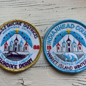 May include: Two embroidered patches with blue and gold trim. The left patch is gold with the text "GESE SKYLINE DISTRICTS 1988 KLONDIKE DERBY" and a depiction of a castle. The right patch is blue with the text "INDIANHEAD COUNCIL 1988 HARRIET ISLAND WINTER CAMP" and a depiction of a castle.