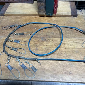 May include: A vintage fishing stringer with multiple metal clips and a blue cord. The stringer is designed to hold fish after they are caught. The metal clips are attached to the cord with swivels.