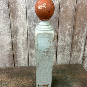 May include: A white wooden post with a rounded terracotta top. The post has a distressed, weathered look with chipped paint.