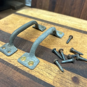 May include: Two antique silver door handles with brass accents on a wooden surface. The handles are in a traditional style with a curved shape. There are several screws scattered around the handles.
