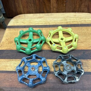 May include: Four vintage water valve handles. Two are green, one is yellow, and one is blue. They are all made of metal and have a starburst design.