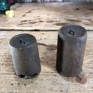 May include: Two rusty metal weights with a loop at the top. The weights are cylindrical and have a rough texture.