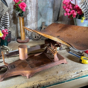 May include: A vintage rusty metal scale with a large, curved platform. The scale has a wooden base and a metal arm with a weight on one end.
