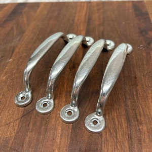 May include: Four silver drawer pulls with a rounded, curved shape. The pulls have a smooth, polished finish and are designed for use on cabinets or drawers.