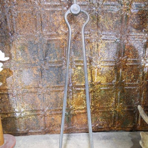 May include: A pair of antique metal fireplace tongs with a black finish. The tongs have a long, slender design and a knob at the top.