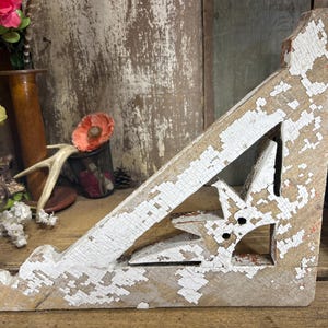 May include: White painted wooden shelf bracket with a decorative cutout design. The bracket has a distressed look with chipped paint and exposed wood.