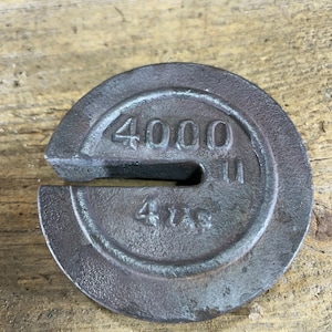May include: A circular, dark metal weight with a cut-out section. The weight is marked with the number "4000" and "4 lbs" in raised lettering. The weight has a worn, aged appearance.