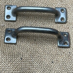 May include: Two silver-toned metal cabinet door pulls with square plates and rounded handles.