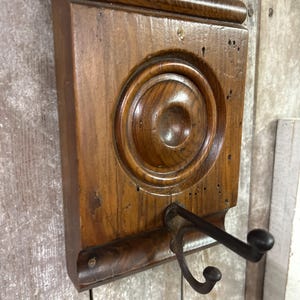 May include: A wooden wall hook with a decorative round design and a single metal hook. The hook is brown and has a distressed finish.