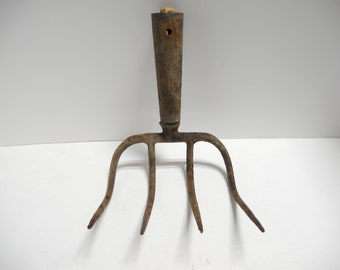 May include: A rusty, vintage garden fork with four curved tines and a wooden handle. The handle has a hole near the top. The tool is made of metal and wood, and is likely used for gardening or farming.