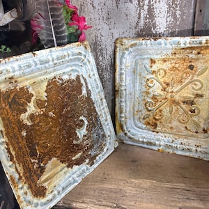 May include: Two square, metal ceiling tiles with a raised, ornate design. The tiles are rusty and have a light blue paint finish.