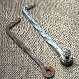 May include: Two antique metal hooks, one with a white painted finish and the other with a rusty brown finish. Both hooks are twisted and have a unique shape.
