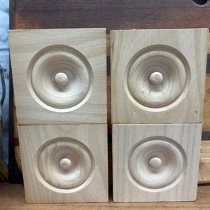 May include: Four unfinished wooden squares with a circular design carved into the center of each. The squares are arranged in two rows of two.