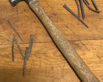 May include: A vintage claw hammer with a wooden handle and a set of rusty nails on a wooden surface.