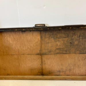 May include: A rectangular wooden box with a hinged lid. The box is made of light brown wood with darker areas and a metal clasp. The box has a simple, rustic design.