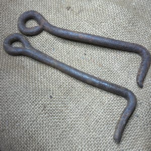 May include: Two rusty metal hooks with a loop at the top. The hooks are bent at a 90-degree angle.