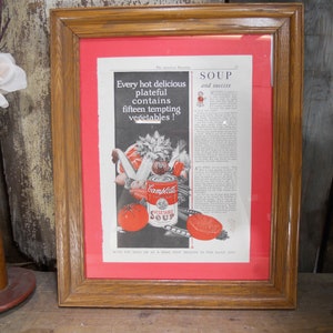 May include: A framed vintage advertisement for Campbell's Vegetable Soup. The ad features a colorful illustration of a can of soup and various vegetables. The text reads "Every hot delicious plateful contains fifteen tempting vegetables!" and "Soup and success".