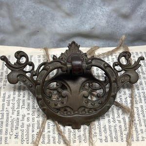 May include: A vintage ornate brass door pull with a decorative scroll design. The pull is attached to a book with twine.