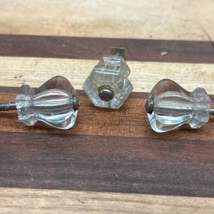 May include: Three vintage clear glass cabinet knobs with metal screws. The knobs have a faceted design and are in good condition.