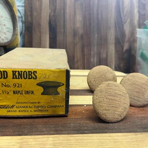 May include: A box of wood knobs labeled "Wood Knobs 1 1/2" No. 921 2 doz. 1 1/2" Maple Unfin."  Manufactured by Waddell Manufacturing Company Grand Rapids 2, Michigan.  Three wooden knobs are shown on a wooden surface.