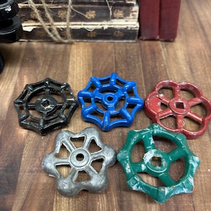 May include: A collection of vintage valve handles in various colors, including black, blue, red, silver, and green. The handles have a star-like design with a central hole and are arranged on a wooden surface.
