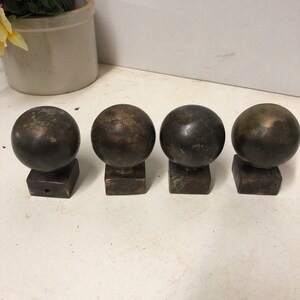 May include: Four dark brown metal finials with square bases. Each finial has a round top and a slightly textured surface.
