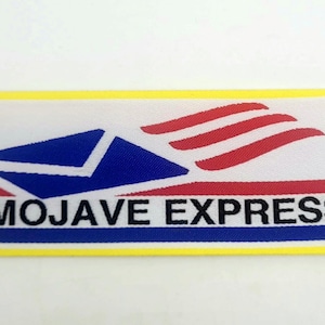 May include: A rectangular patch with a yellow border. The patch features a blue envelope design and red stripes, with the words "MOJAVE EXPRESS" in black. The background is white.