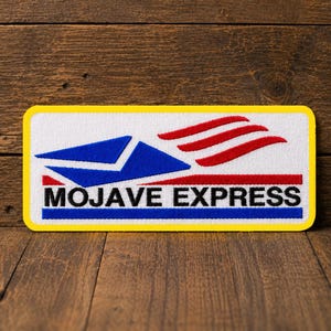 Puede incluir: Un parche rectangular bordado con un borde amarillo. El diseño presenta un icono de sobre azul, tres líneas curvas rojas y el texto negro MOJAVE EXPRESS centrado sobre una línea roja fina y una línea azul sobre un fondo blanco.
