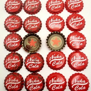 Peut inclure: Une collection de 18 capsules de bouteille rouges avec les mots "Nuka Cola" imprimés en blanc. Les capsules de bouteille sont disposées en grille sur une surface blanche.