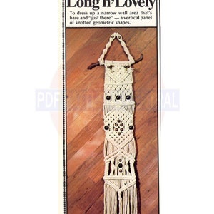 Puede incluir: Un tapiz de macramé blanco con cuentas de madera marrón. El tapiz tiene la forma de un rectángulo largo con una parte superior puntiaguda. El tapiz está sobre un suelo de madera.