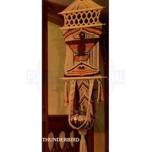 May include: A macrame plant hanger with a brown and orange geometric design. The hanger is made of natural fibre rope and has a tassel at the bottom. The word "THUNDERBIRD" is printed below the hanger.