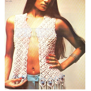 Op de afbeelding: Een wit gebreid vest met blauwe kralen en franjes. Het vest is open aan de voorkant en heeft een diepe V-hals.