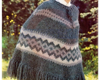 Op de afbeelding: Een groene, blauwe en roze gebreide poncho met franjes. De poncho heeft een geometrisch patroon en wordt gedragen door een vrouw met blond haar.
