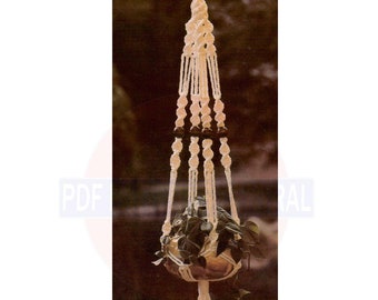 May include: White macrame plant hanger with a brown pot and green plant. The hanger has a tassel at the bottom and the text "Bordeaux" is visible below the pot.