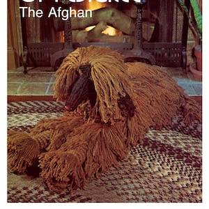 Peut inclure: Un jouet en peluche représentant un lévrier afghan brun et noir avec une fourrure longue et hirsute. Le jouet est couché sur un tapis à motifs devant une cheminée.