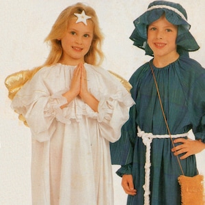 May include: Two children dressed in costumes for a nativity play. A girl is wearing a white angel costume with gold wings and a star on her forehead. A boy is wearing a blue robe with a white rope belt and a brown pouch.