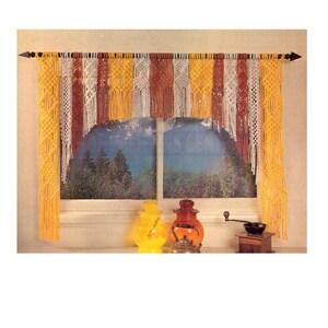 May include: A macrame window valance with a scalloped bottom edge. The valance is made with yellow, white, and brown yarn and is hung on a black rod.