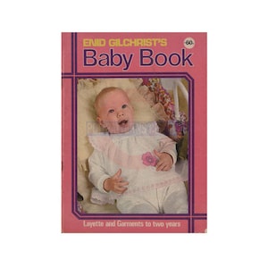May include: A pink book cover with the title "Enid Gilchrist's Baby Book" and a photo of a baby wearing a white knitted outfit with a pink flower.