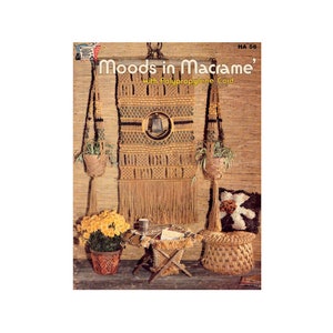 May include: A book titled "Moods in Macrame' with Polypropylene Cord" with a picture of a macrame wall hanging, a macrame stool, and a macrame footstool. The wall hanging is made with natural colored cord and has a bell in the center. The stool and footstool are also made with natural colored cord.