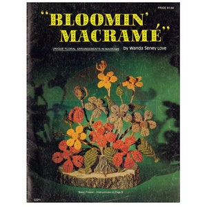 May include: A vintage book cover with a green background and a macrame flower arrangement in shades of orange, yellow, and brown. The title of the book is "Bloom'n Macrame" and the subtitle is "Unique Floral Arrangements in Macrame" by Wanda Seney Love.