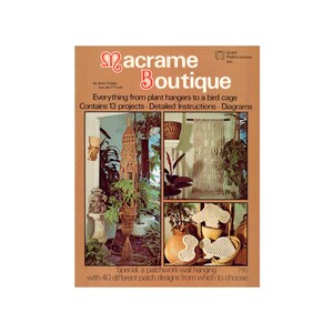 May include: A book cover for a macrame craft book titled "Macrame Boutique" by Betti Hodges and Joe O'Toole. The cover features three photos of macrame projects: a plant hanger, a wall hanging, and a bird cage. The book contains 13 projects, detailed instructions, and diagrams. It also includes a special patchwork wall hanging with 40 different patch designs.