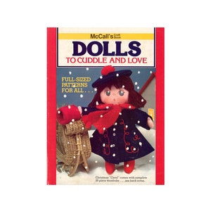 May include: A craft book cover titled "Dolls to Cuddle and Love". The cover features a doll wearing a blue coat, red scarf, and a black beret. The doll is holding a red basket and is standing in a snowy scene. The text "Full-Sized Patterns for All" is printed on the cover.