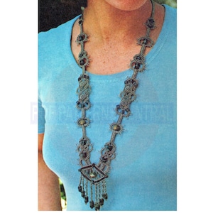May include: A gray and brown macrame necklace with black beads. The necklace has a pendant with a fringe.
