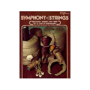 May include: A book titled "Symphony of Strings: Macrame Jewelry and Belts for a Look of Individuality" by Gura Round, Liz Barfell, Thory Willin. The cover features a close-up of various macrame jewelry pieces and cords.