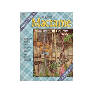 May include: A book cover for a macrame craft project featuring a rustic stone wall background with three macrame plant hangers. The book title is "PLAID'S Macrame Macrame For Country Living" and the author is "BY SANDY DYE".