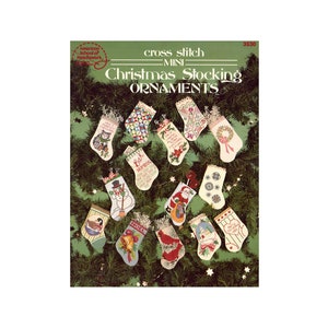 May include: A cross stitch pattern booklet featuring 12 mini Christmas stocking ornaments. The cover shows the stockings hanging on a green garland with red berries and gold stars.